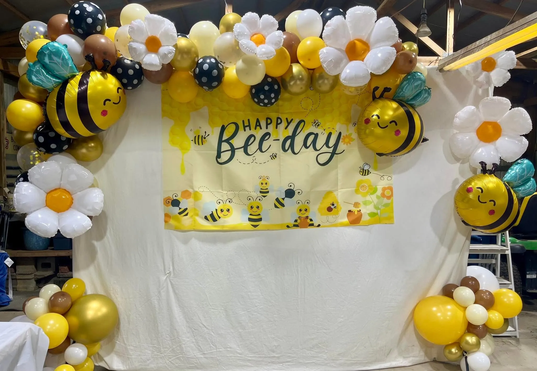 Garland of yellow, gold, cream, brown and polka-dot balloons with bee and daisy foils framing a Happy Bee-Day backdrop