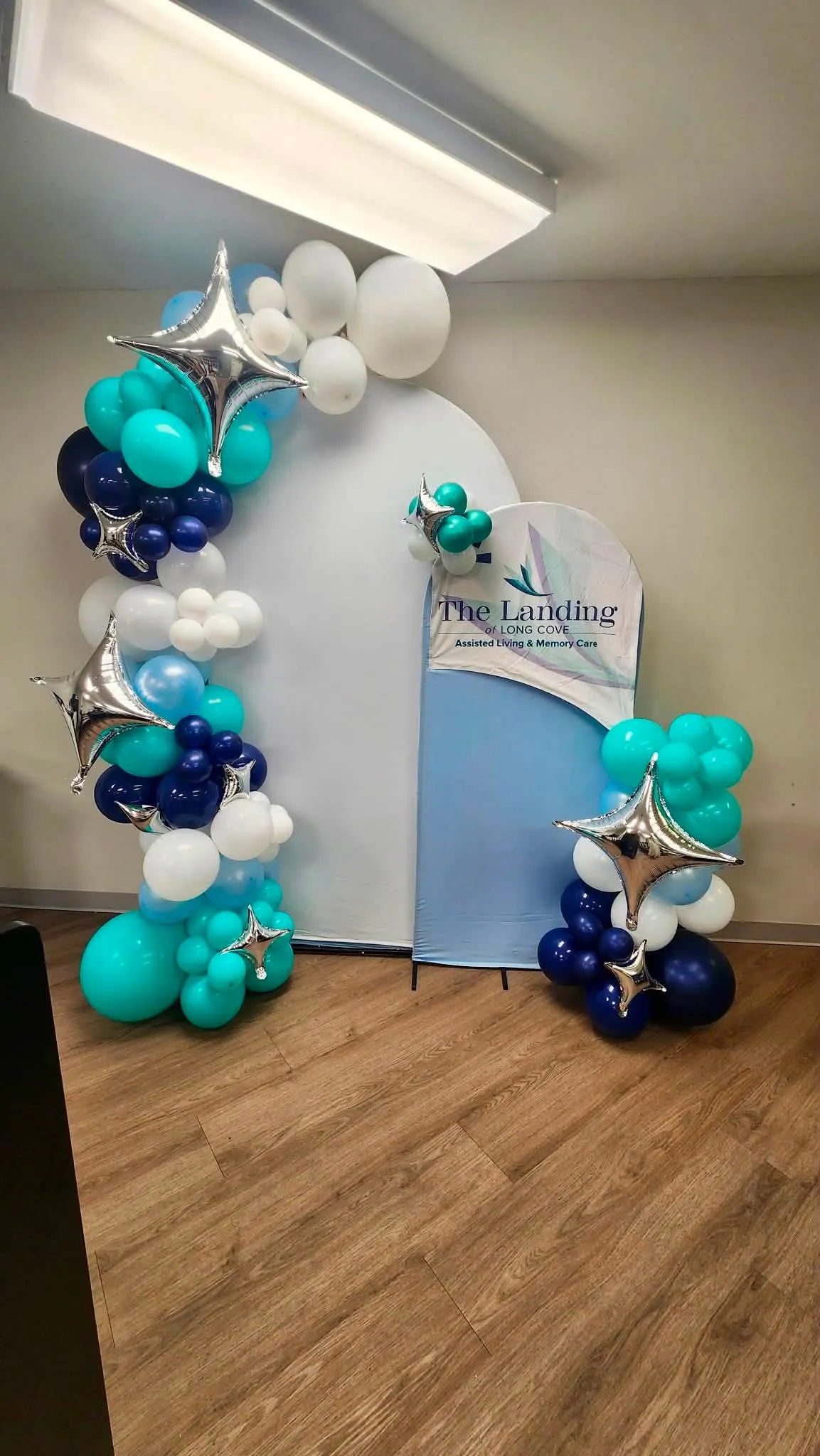 Teal, navy, baby blue and white balloon garland with silver star foils around white and blue arch backdrops with a business sign
