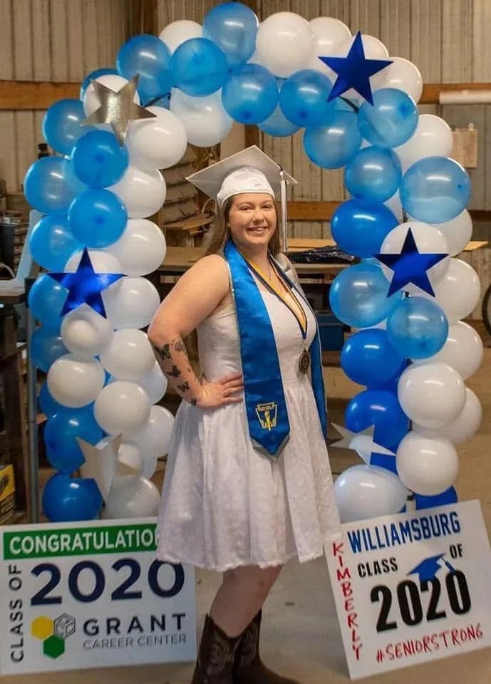 Blue and white balloon arch with blue and silver star foils around a graduate in a cap and stole