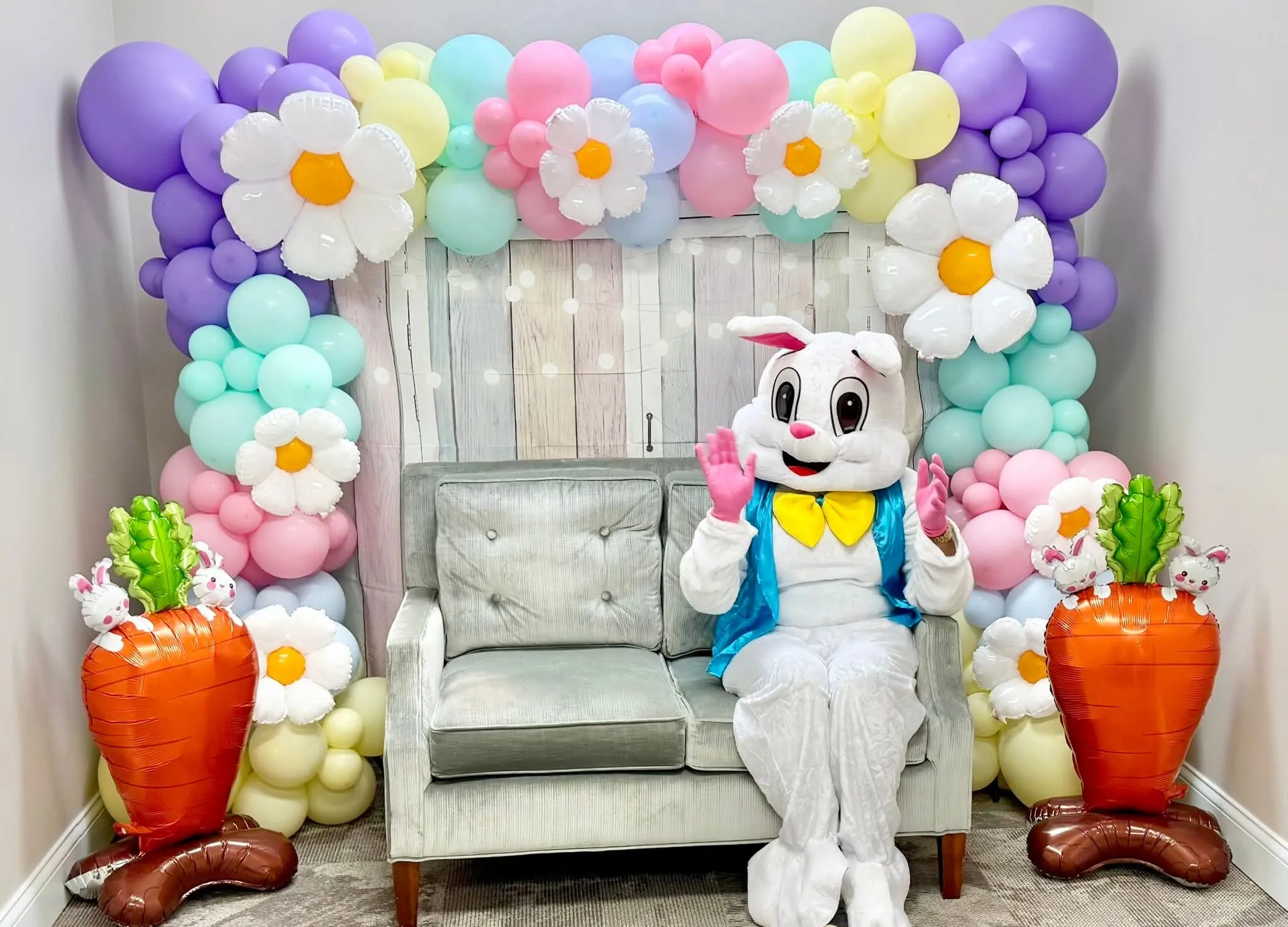 Easter Bunny waving from a loveseat inside a pastel daisy balloon garland