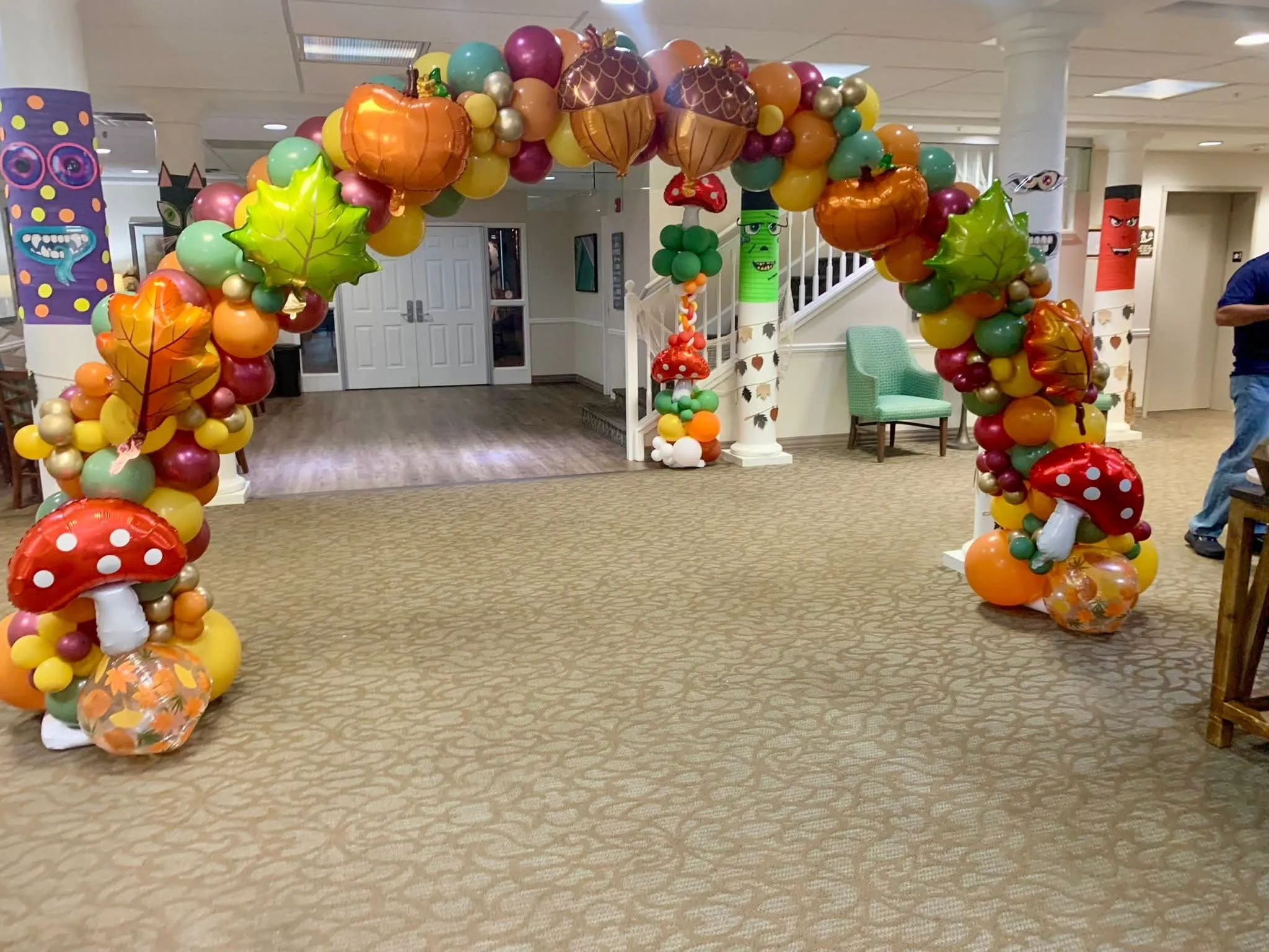 Walk-through fall balloon arch in orange, sage, burgundy and gold with pumpkin, acorn, leaf and mushroom foil balloons