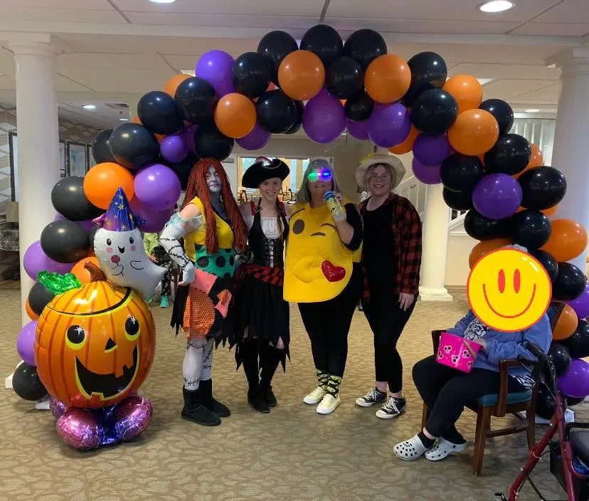 Black, orange and purple balloon arch with a ghost and a large jack-o’-lantern balloon, with four people in costume underneath