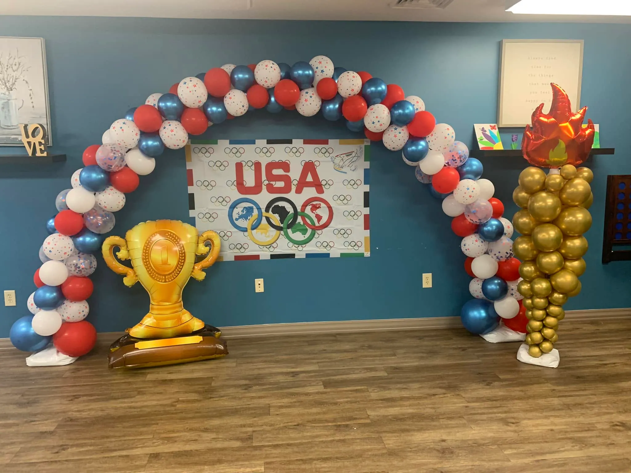 Red, white, chrome blue and star-print balloon arch over a USA banner, with a trophy balloon and a gold balloon torch column