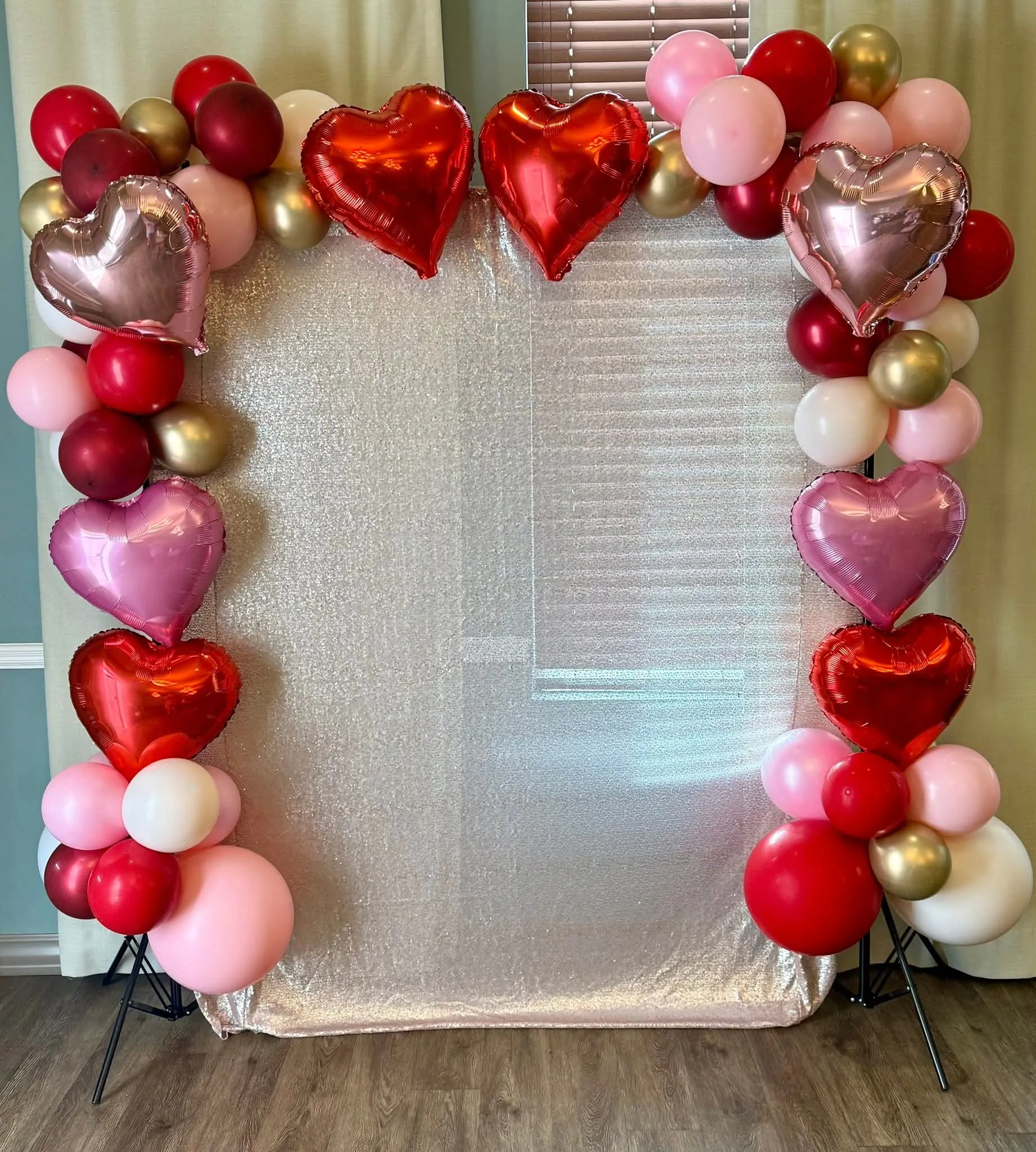 Red, pink, burgundy and gold balloon garland with red and pink heart foil balloons framing a shimmer backdrop