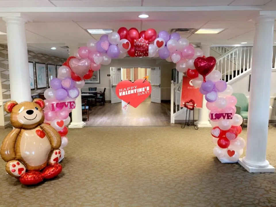 Arch of pink, red, lilac and pearl balloons with heart prints and I Love You foils, beside a giant teddy bear balloon