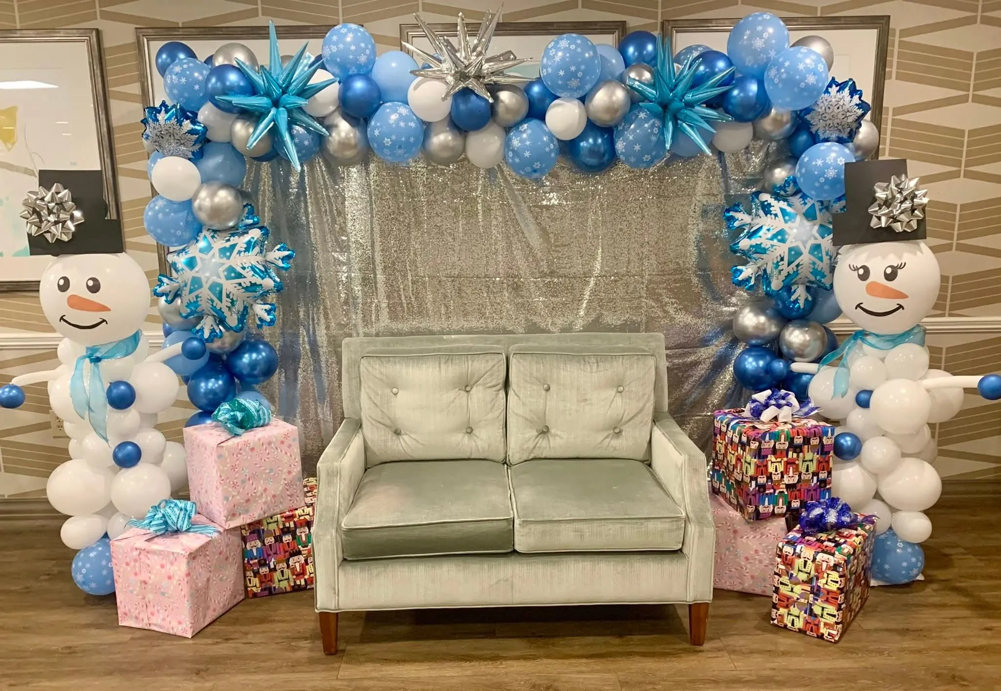 Winter wonderland photo booth with blue, white and silver balloon garland, snowflake balloons, balloon snowmen and wrapped gifts